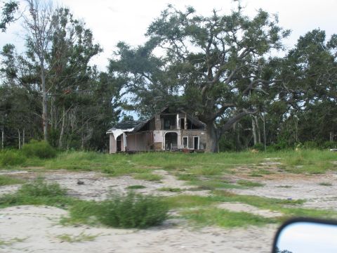 1995 Ford C-350 (Centurion Conversions) - A house severely damaged by a storm, with trees in the background.