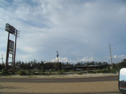 1995 Ford C-350 (Centurion Conversions) - The aftermath of a disaster shows damaged structures and debris under a partly cloudy sky.