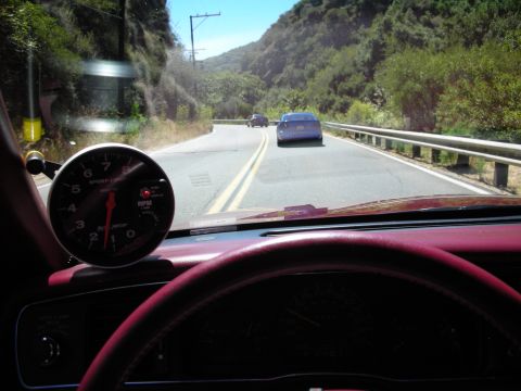1998 Ford Crown Victoria - Driver's-eye view over a red dashboard and mounted tachometer, following cars on a winding canyon road through the windshield.