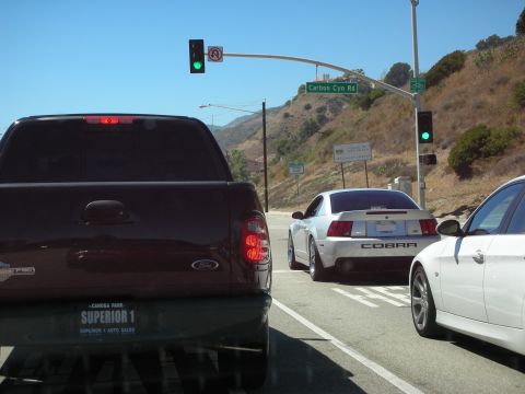 1998 Ford Crown Victoria - silver Mustang Cobra and a white car wait at a green-lit intersection behind a maroon Ford pickup near Carbon Canyon Road.