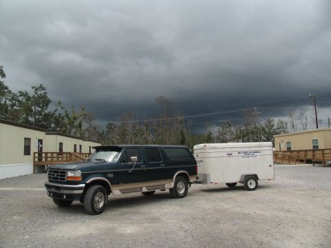 1995 Ford C-350 (Centurion Conversions) - A Ford Bronco tows a trailer in front of modular buildings under a dark, stormy sky.