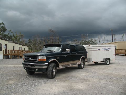 1995 Ford C-350 (Centurion Conversions) - A dark green Ford SUV tows a white trailer under a stormy sky.