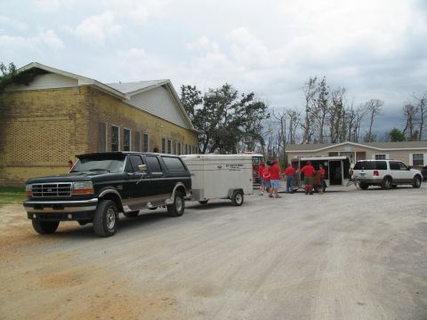 1995 Ford C-350 (Centurion Conversions) - A 1995 Ford F-Series truck is seen towing a trailer, with a white SUV and several people in the background.