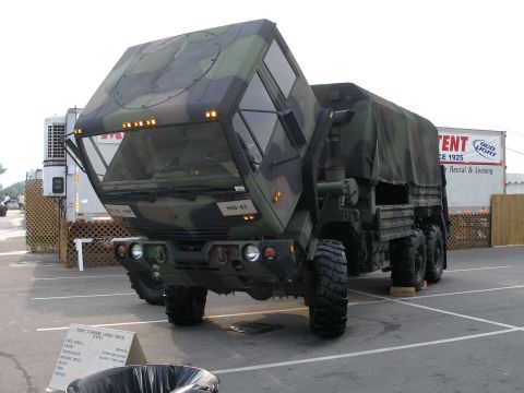 1998 Ford Crown Victoria - A woodland-camouflage 6x6 military cargo truck on display in a paved lot with its cab tilted forward for engine access, marked "HHD-82" on…
