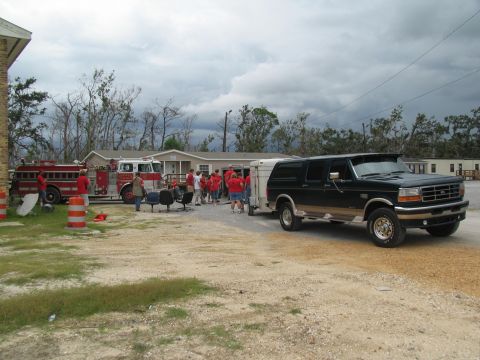 1995 Ford C-350 (Centurion Conversions) - A dark green Ford Bronco tows a trailer, with fire trucks and people in red shirts nearby.