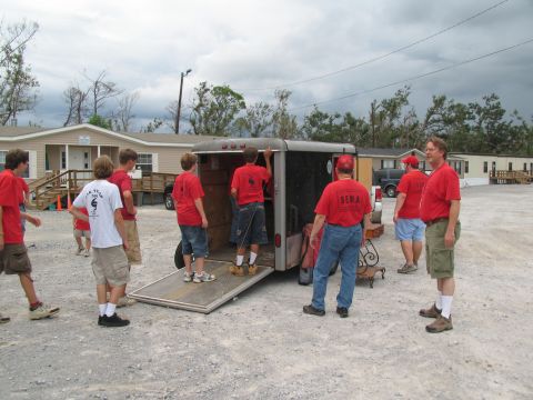 1995 Ford C-350 (Centurion Conversions) - Volunteers unload supplies from a trailer in front of temporary housing units.
