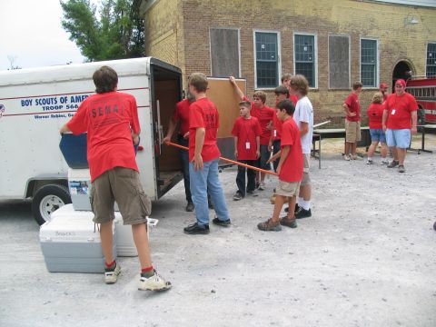 1995 Ford C-350 (Centurion Conversions) - A group of Boy Scouts are seen unloading supplies from a trailer next to a brick building.