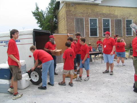 1995 Ford C-350 (Centurion Conversions) - People in red shirts are seen unloading supplies from a trailer in front of a brick building.