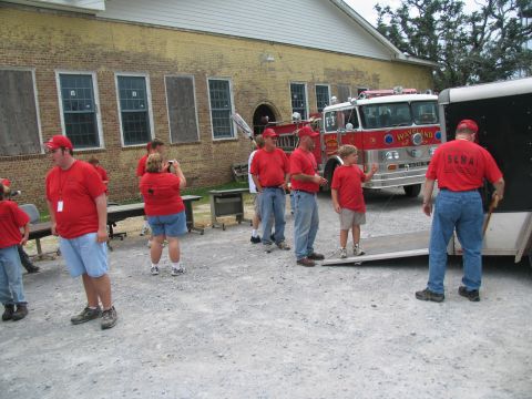 1995 Ford C-350 (Centurion Conversions) - A red fire truck is parked in front of a brick building, with several people in red shirts standing nearby.