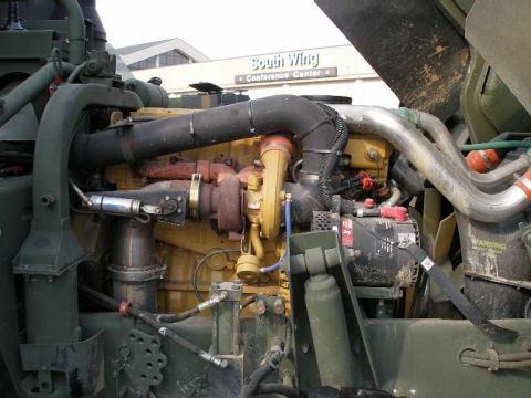 1998 Ford Crown Victoria - Engine-bay view of a large olive-drab military cargo truck showing a yellow Caterpillar diesel engine with its turbocharger, exhaust piping…