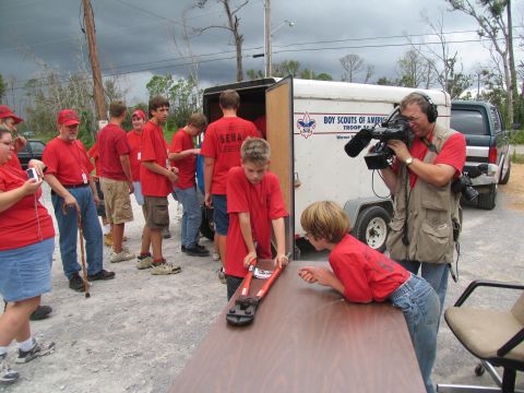 1995 Ford C-350 (Centurion Conversions) - A group of people, some wearing red shirts with 'SEMA' on them, are gathered near a trailer and a pickup truck. A cameraman is filming the…