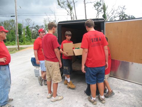 1995 Ford C-350 (Centurion Conversions) - Volunteers unload boxes from a trailer, with one person wearing a shirt that says SEMA.