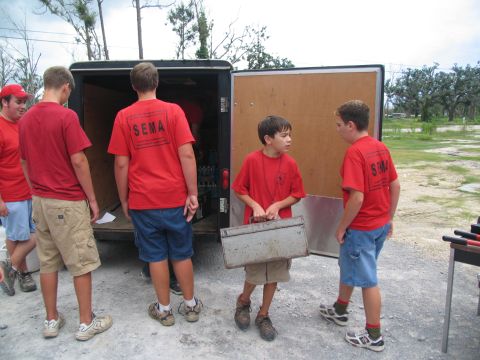 1995 Ford C-350 (Centurion Conversions) - Boys in red SEMA shirts are seen unloading supplies from a trailer.