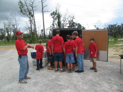 1995 Ford C-350 (Centurion Conversions) - Volunteers in red shirts with 'SEVA' on the back unload supplies from a trailer.