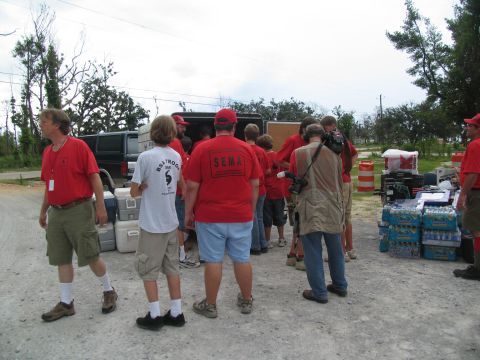 1995 Ford C-350 (Centurion Conversions) - People wearing red shirts are gathered around supplies, with a van visible in the background.