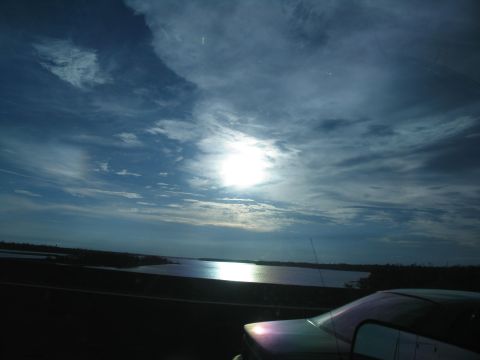1995 Ford C-350 (Centurion Conversions) - A car is parked on the side of a road next to a large body of water under a cloudy sky.