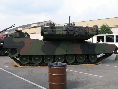 1998 Ford Crown Victoria - Side profile of a woodland-camouflage (green, brown, black) main battle tank displayed outdoors, with a long main gun barrel, seven road wh…