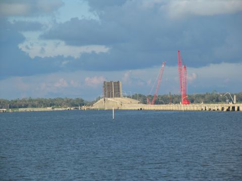 1995 Ford C-350 (Centurion Conversions) - A bridge under construction is visible with two large red cranes operating nearby, set against a cloudy sky.