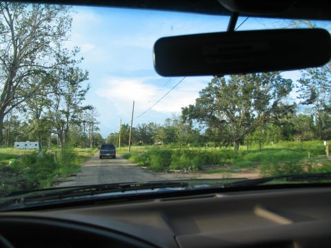 1995 Ford C-350 (Centurion Conversions) - Driving down a rural dirt road with a single vehicle ahead and trees lining the path.