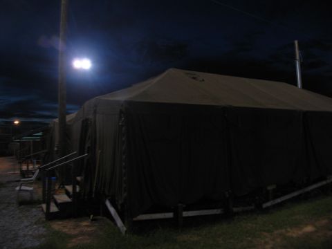 1995 Ford C-350 (Centurion Conversions) - Temporary shelters are set up, likely for disaster relief, under a dark sky with bright floodlights.