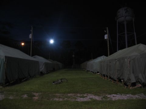 1995 Ford C-350 (Centurion Conversions) - Military tents are set up in rows at night, with a water tower visible in the distance.