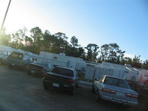 1995 Ford C-350 (Centurion Conversions) - Several cars are parked in a lot with trailers and trees in the background.