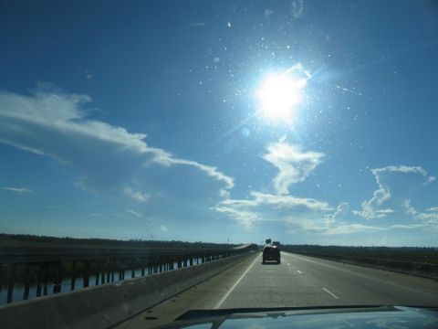 1995 Ford C-350 (Centurion Conversions) - Driving on a highway with a bright sun and scattered clouds overhead. Another vehicle is visible in the distance.