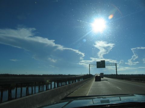1995 Ford C-350 (Centurion Conversions) - View from a vehicle driving on a highway bridge under a bright sun and blue sky with clouds.