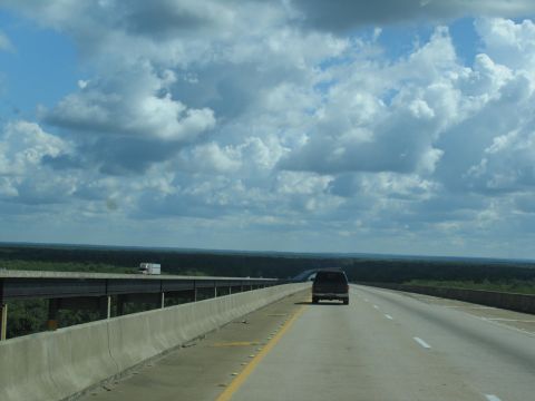 1995 Ford C-350 (Centurion Conversions) - A dark SUV travels down a highway under a cloudy sky.