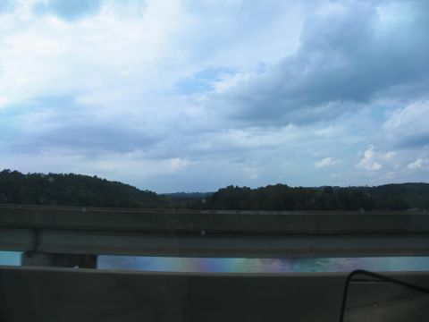 1995 Ford C-350 (Centurion Conversions) - A view from a bridge shows a concrete barrier overlooking a body of water with a rainbow sheen, under a cloudy sky.