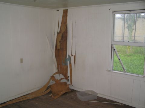1995 Ford C-350 (Centurion Conversions) - The interior of a room shows significant damage to the wall paneling, exposing the underlying wood structure.