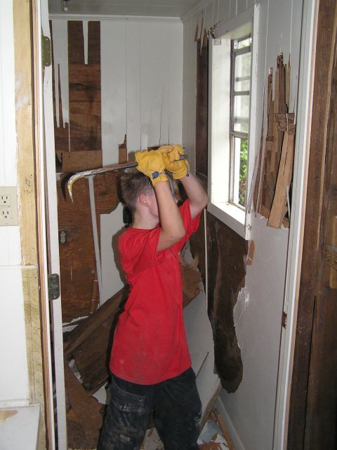 1995 Ford C-350 (Centurion Conversions) - A person is actively demolishing the interior of a room, tearing down wall panels with a crowbar.