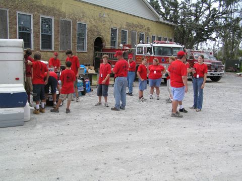1995 Ford C-350 (Centurion Conversions) - People in red shirts stand near red fire trucks outside a yellow brick building, possibly a fire station.