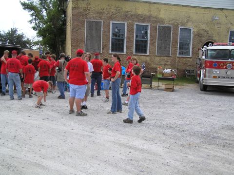 1995 Ford C-350 (Centurion Conversions) - A fire truck is visible next to a brick building where a group of people in red shirts are gathered.