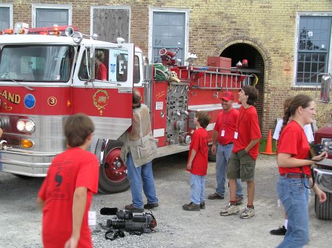 1995 Ford C-350 (Centurion Conversions) - A group of people, some wearing red shirts, stand near a large red fire truck.