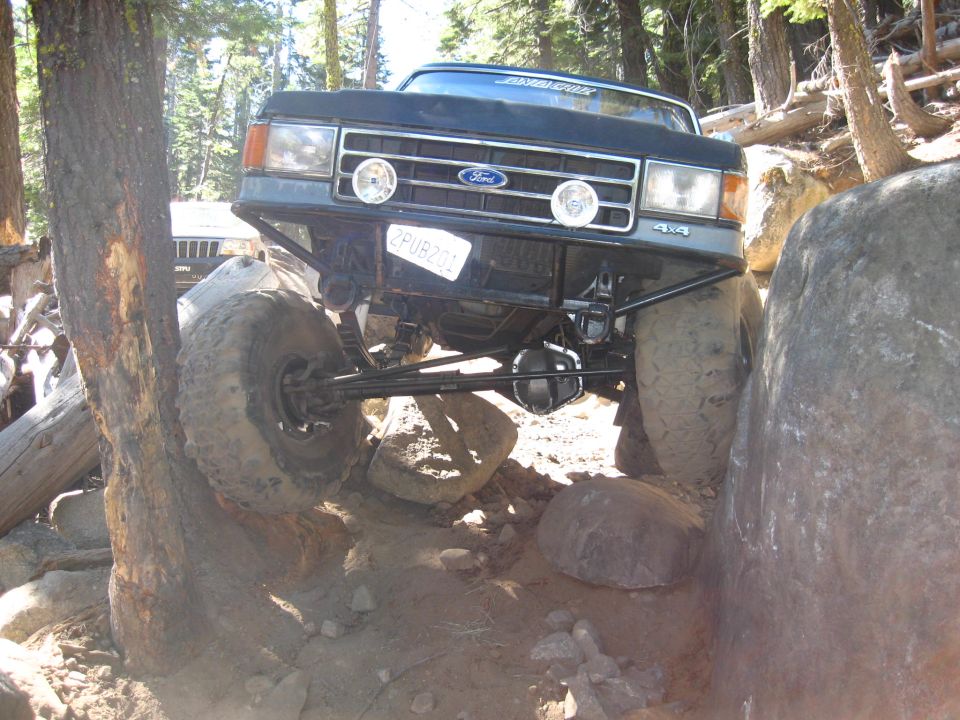 Modified Ford truck with large tires navigating rocks; another SUV visible behind
