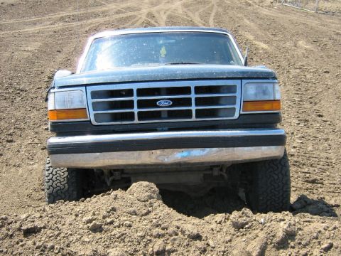 1995 Ford Bronco - This Ford truck is stuck in a dirt mound, showing its front grille and tires.