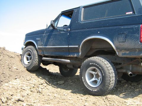1995 Ford Bronco - A dark blue Ford Bronco is shown from the side, climbing a dirt incline with BFGoodrich tires.