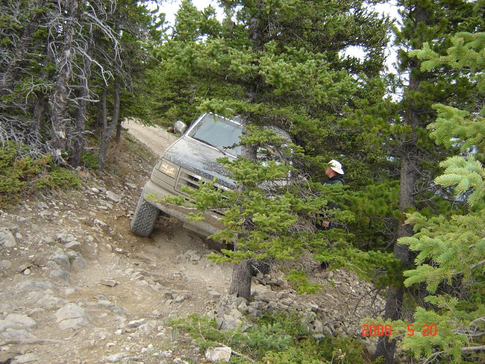 Ford Bronco navigating a steep, rocky off-road trail surrounded by trees