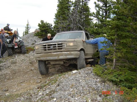 1995 Ford Bronco - A tan Ford Bronco navigates a rough, rocky trail with people nearby.