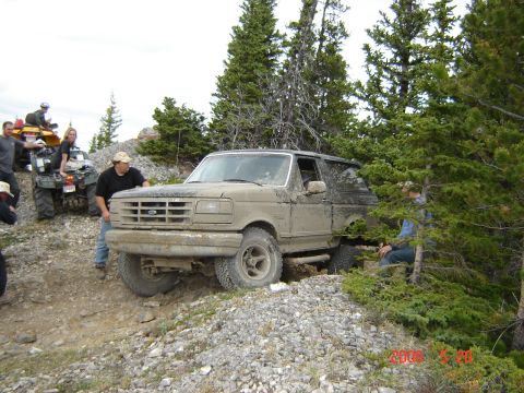 1995 Ford Bronco - A muddy 1995 Ford Bronco navigates a rocky trail, with ATVs and people nearby.