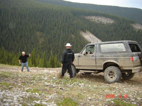 1995 Ford Bronco - Two men stand near a dirty Ford Bronco on a mountain path, surrounded by dense forest.