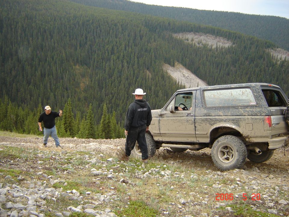 Muddy 1992 Ford Bronco parked on a rocky mountain trail with two people nearby