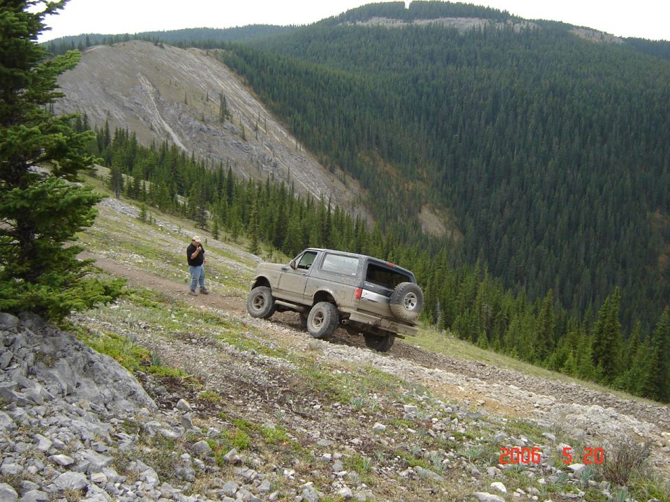 Tan Ford Bronco on a dirt road, rear view. Spare tire mounted on the back