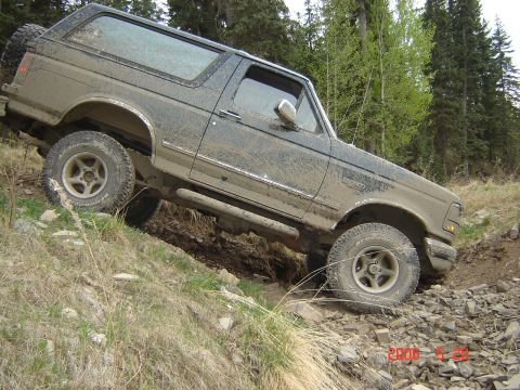 1995 Ford Bronco - A muddy 1992 Ford Bronco navigates a challenging off-road trail with steep inclines and loose rocks.