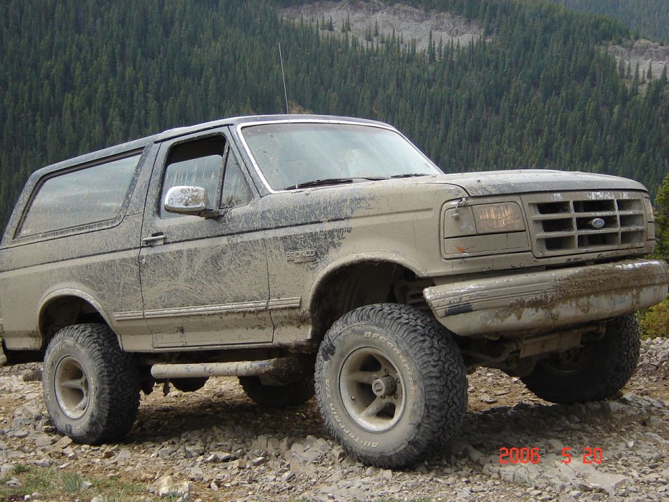 Mud-covered 1995 Ford Bronco parked on a rocky, off-road trail with a forest in the background