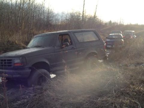 1995 Ford Bronco - A dark 1995 Ford Bronco is stuck in the mud, with other vehicles following behind on a trail.
