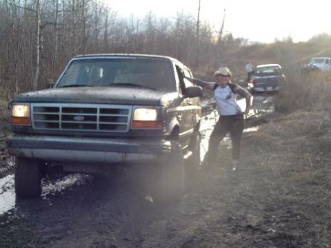1995 Ford Bronco - A group of vehicles navigate a muddy off-road course with trees in the background.