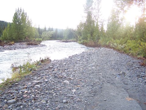 1979 Chevrolet Blazer - A wide river flows alongside a rocky bank and a gravel road, with trees lining the horizon.