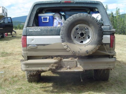 1995 Ford Bronco - The rear of a muddy Ford Bronco is shown with a spare tire and camping gear inside.